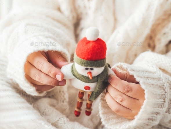 Kid with felt decorative snowman for Christmas tree. Boy in cable-knit oversized sweater.