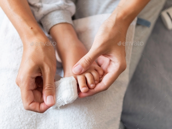 Mother bandages her child\'s big toe. First aid in case of small domestic injury.