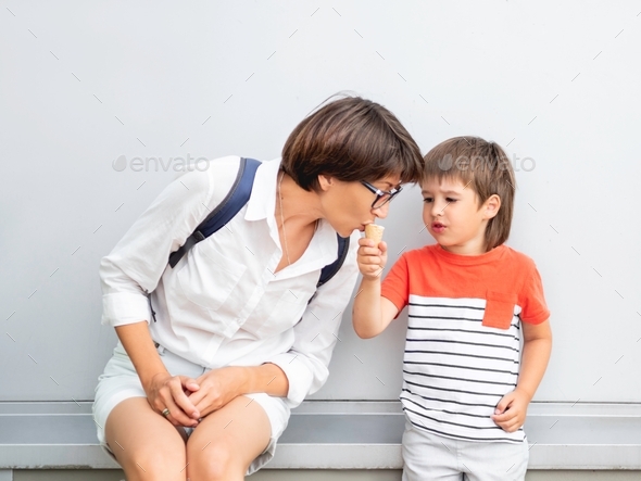 Little boy shares ice-cream with his mother. Mom and son eat cold dessert outdoors. Summer vibes.