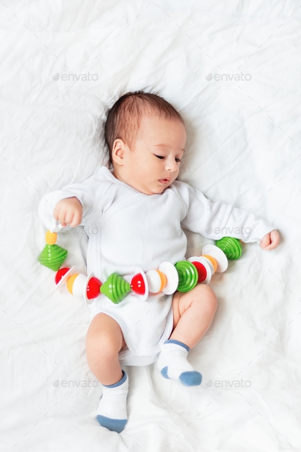 Baby boy holds colorful rattle toy. Top view of little kid lying with his first toy.