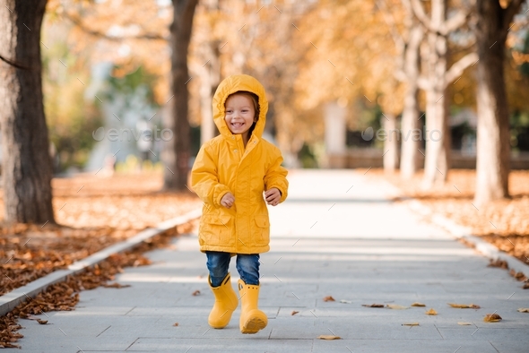Smiling happy little girl wear yellow raincoat and rubber boots run in park. Happiness. Cheerful kid