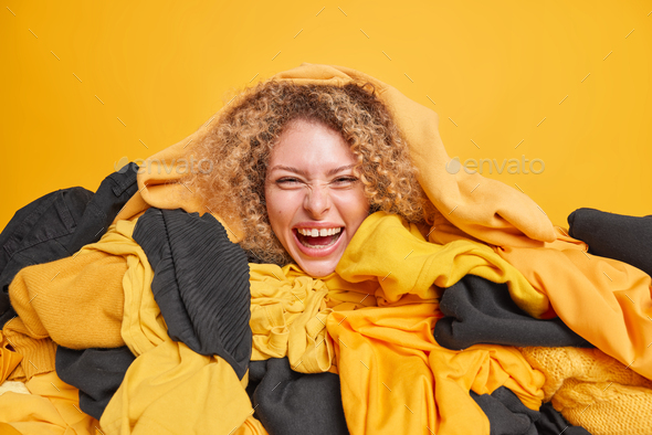Daily housekeeping work concept. Joyful curly haired young woman sorts out clothes organizes closet