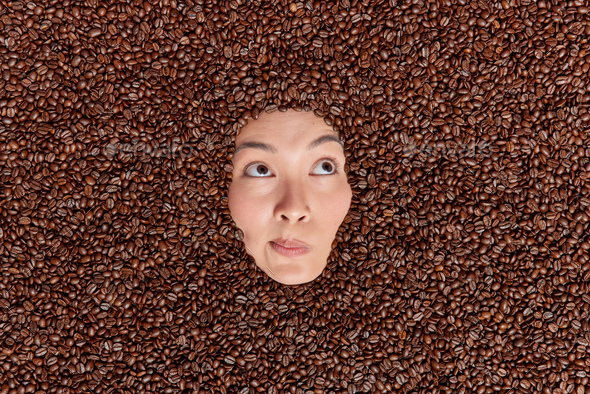 Overhead shot of Asian woman shows only face through coffee beans containing much caffeine which hel