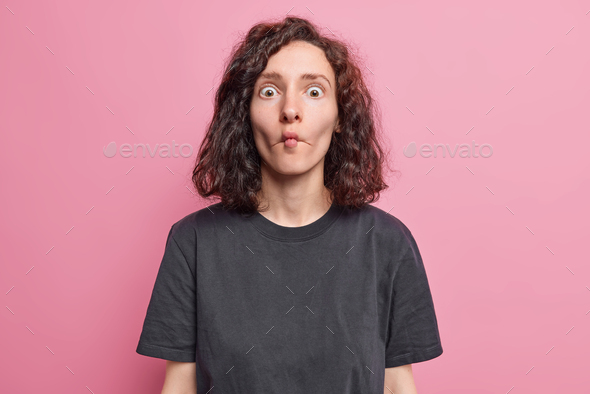 Portrait of funny brunette woman makes fish face with lips comic grimace dressed in casual black t s
