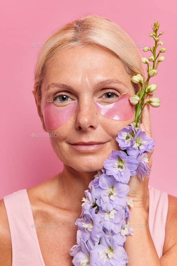Serious middle aged woman moisturizes skin with hydrogel patches has beauty day redyces eye bags hol