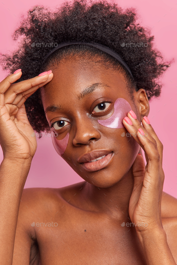 Pretty dark skinned woman with curly hair applies collagen patches under eyes to remove dark circles