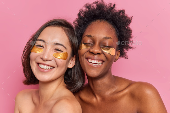 Happy mixed race women friends apply golden collagen patches under eyes to remove dark circles being