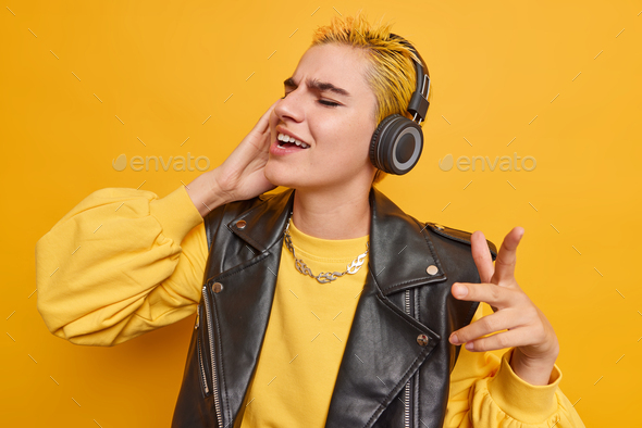 Joyful Caucasian girl with trendy hairstyle listens music in wirelesss headphones catches every bit