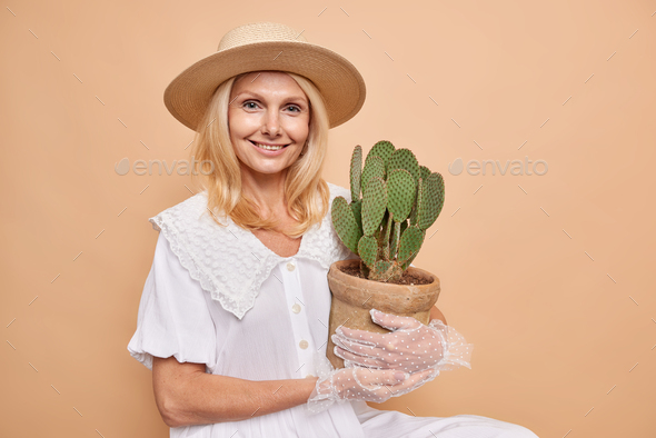 Horizontal shot of good looking lady with aristocractic manners wears stylish outfit carries potted