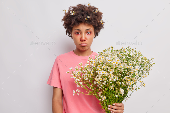 Pollen allergy. Frustrated curly haired woman suffers from allergic symptoms holds bouquet of camomi