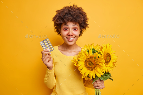Seasonal allergy. Cheerful Afro American woman holds drugs and bouquet of sunflowers suffers from al