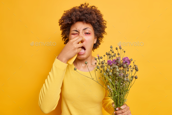 Indoor shot of young Afro American woman suffers from allergic rhinitis uses napkin to blow nose nee