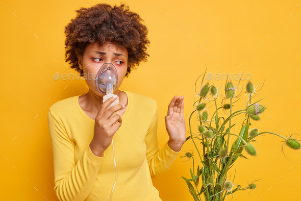 Unhappy dark skinned woman suffers from allergy to wild flowers uses inhalation nebulizer has red wa