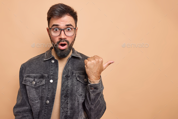 Impressed bearded handsome man points thumb away recommends follow website click on banner gasps fro
