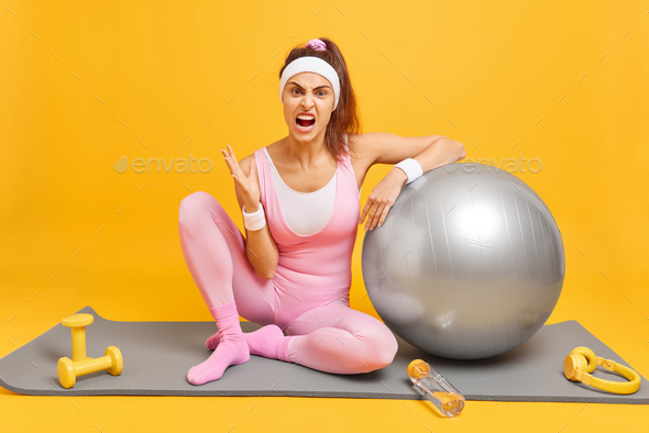 Angry irritated sportswoman in activewear feels annoyed after cardio workout at home poses on fitnes