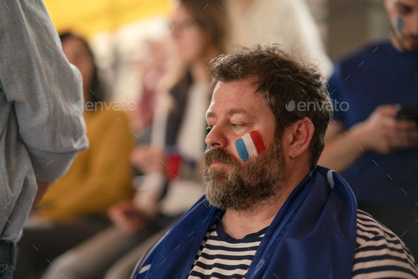 Worried football fans supporting French national team in live soccer match at stadium.
