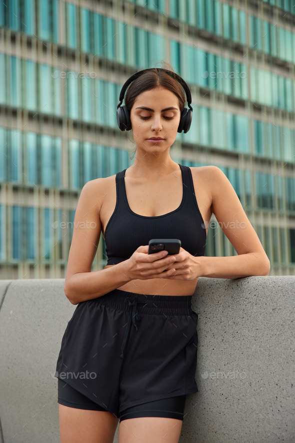 Young sportive woman in sportswear downloads songs to playlist for workout reads news about last com