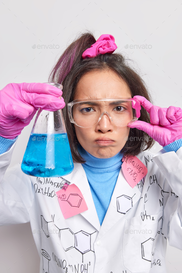 Serious female scientist conducts experiment got blue liquid after mixing chemicals makes test