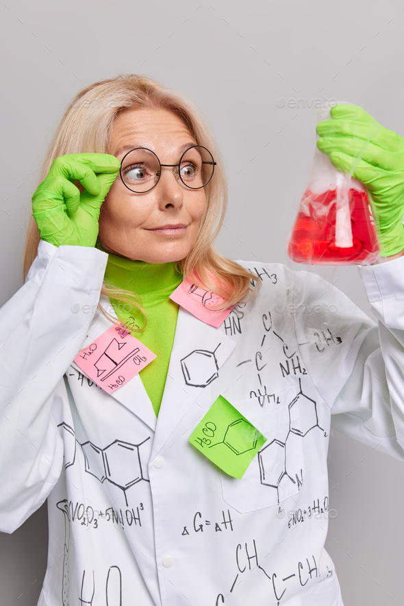Scientific discovery. Surprised female researcher looks at flask with red liquid does research in cl