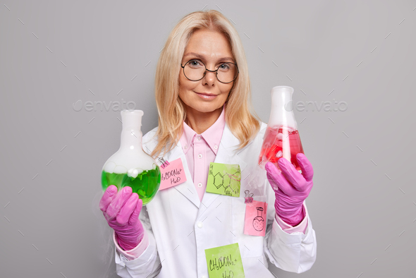 Scientific discovery concept. Self confident middle aged woman chemist makes tests holds glass flask