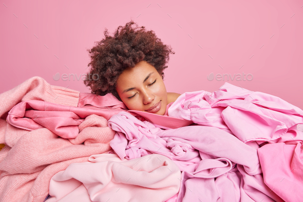 Tired sleepy Afro American woman leans head at pile of laundry feels exhausted after doing housework