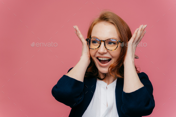 Positive smiling redhead woman covers ears, happy to hear something noisy and funny