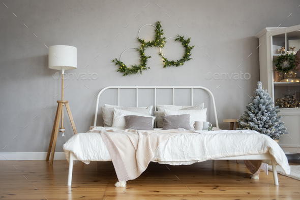 White wrought iron bed with textured milky throws and pillows on wood floor next to Christmas tree.