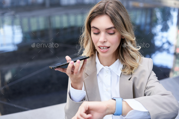Businesswoman checks time on digital watch and records voice message, arranges a meeting, sits