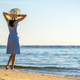 Young woman in straw hat and a dress standing alone on empty sand beach at sea shore - PhotoDune Item for Sale