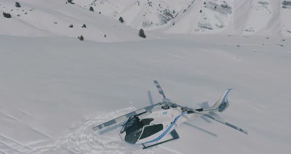 The aerial flies over a parked helicopter standing in the snow in the winter mountains alt