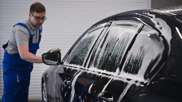 Male Hand in Black Glove Washes Side Mirror of a Black Car alt