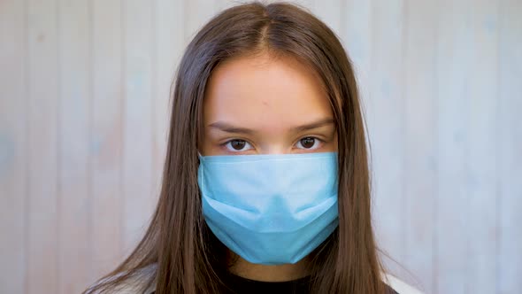 Portrait of Beautiful Brunette Teen Girl in Medical Protective Mask Over Light Gray Wall Background