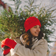 A beautiful girl in a red hat carries a Christmas tree. - PhotoDune Item for Sale