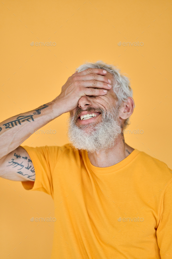Smiling funny older bearded tattooed man laughing isolated on yellow.