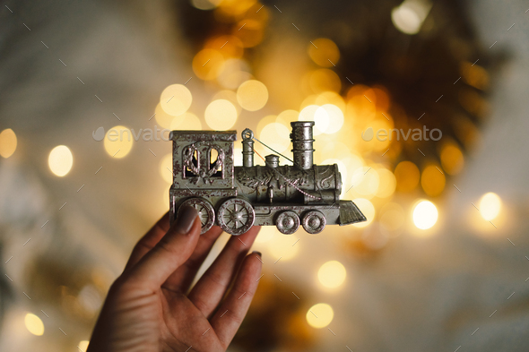 A woman's hand holds a Christmas train on a festive background with golden lights. - Stock Photo - Images