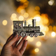 A woman&#39;s hand holds a Christmas train on a festive background with golden lights. - PhotoDune Item for Sale