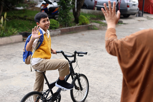 Schoolboy waving hands to mother while riding a bike
