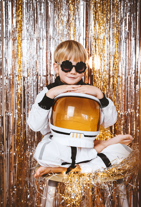 Child in astronaut pilot costume in festive background with foil curtain decorations