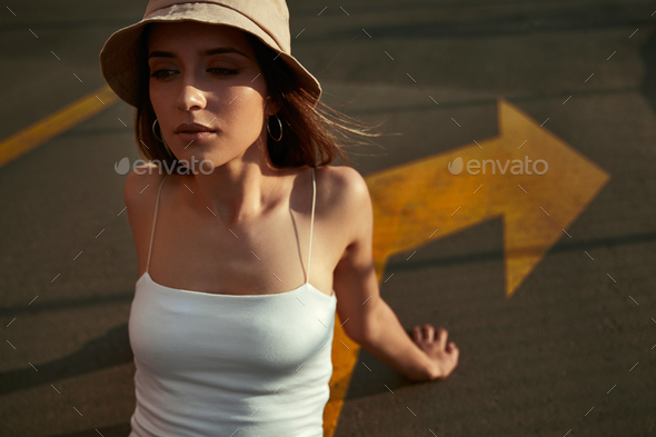 Young woman in hat sitting on road