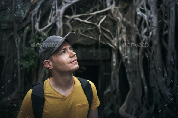 Man admiring overgrown ancient temple under giant roots of tree - Stock Photo - Images