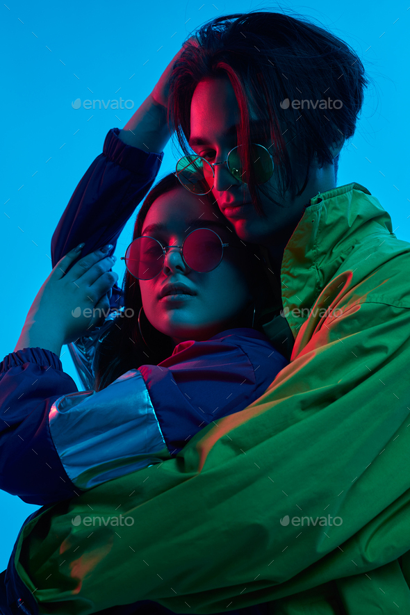 Trendy couple embracing in studio with neon illumination