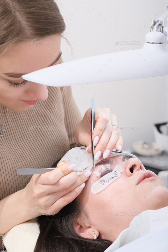 beautiful woman beautician holding tweezers with false lash to glue it to a client's eyelid. - Stock Photo - Images