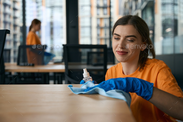 Two female cleaners disinfect furniture in the office with special products