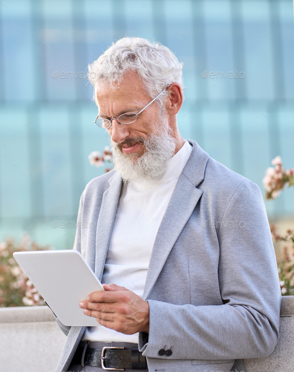 Old senior professional business man using digital tablet standing outdoors. - Stock Photo - Images