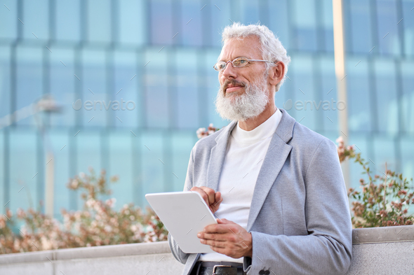 Old senior professional business man using digital tablet thinking outdoors. - Stock Photo - Images