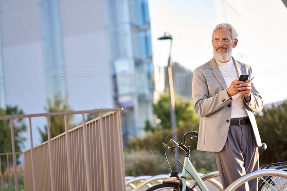 Old senior man using mobile app for bike rental renting bicycle in city park.