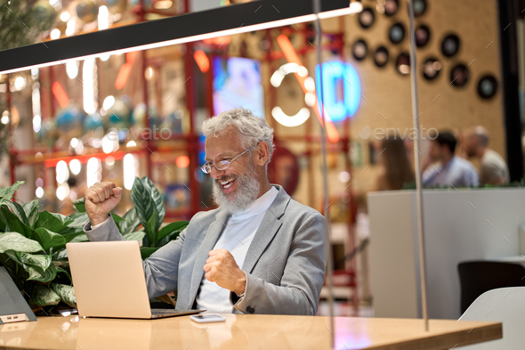 Happy old senior business man investor looking at laptop celebrating profit.