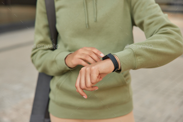 Cropped shot of unknown woman checks fitness results on smartwatch monitors pulse dressed in casual