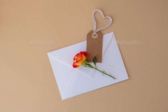 Beautiful red roses flowers in postal envelope on neutral beige background, beige paper note with