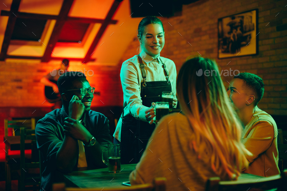 Young happy waitress serving beer to group of customers in a bar.